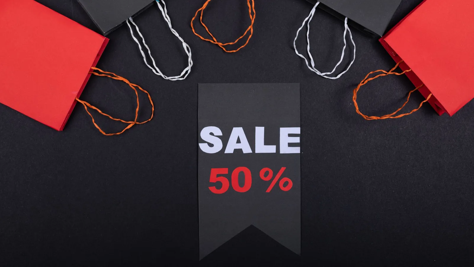 Red and black paper shopping bags around a black tag reading Sale 50%