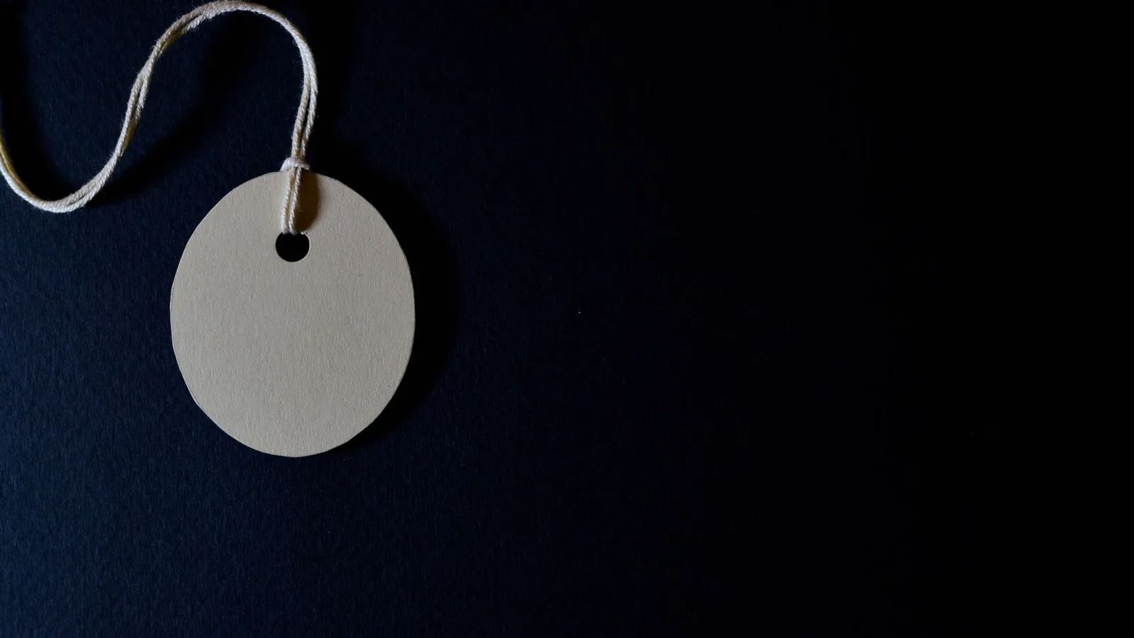 Blank paper price tag on a string against a dark navy background