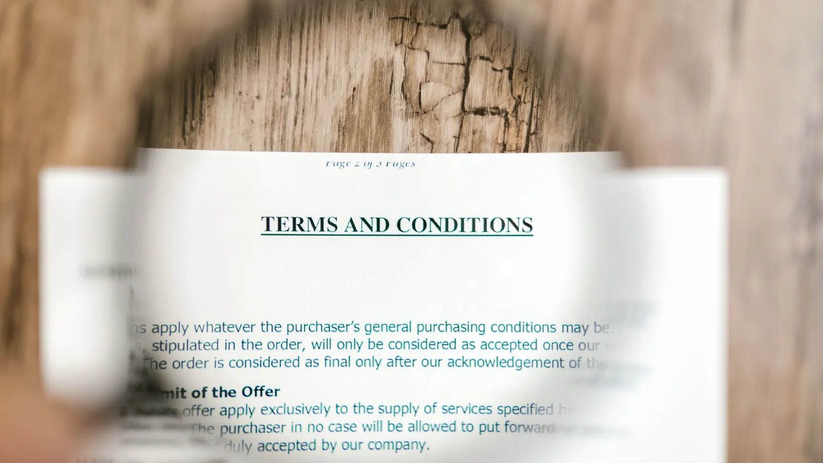 Magnifying glass over a printed terms and conditions document on a wooden surface